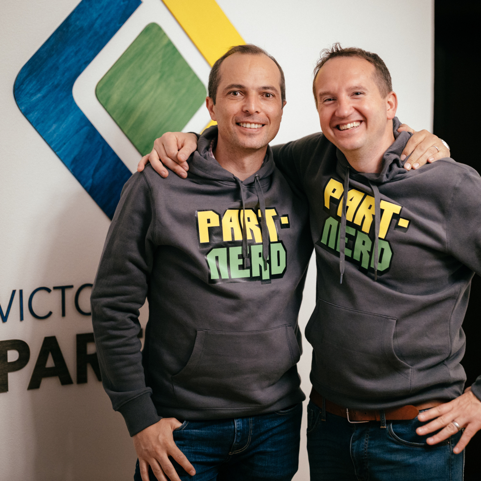 Co-founders of sofware engineering company Victory Square Partners in front of the logo. Both are wearing company hoodies with the text Part.nerds
