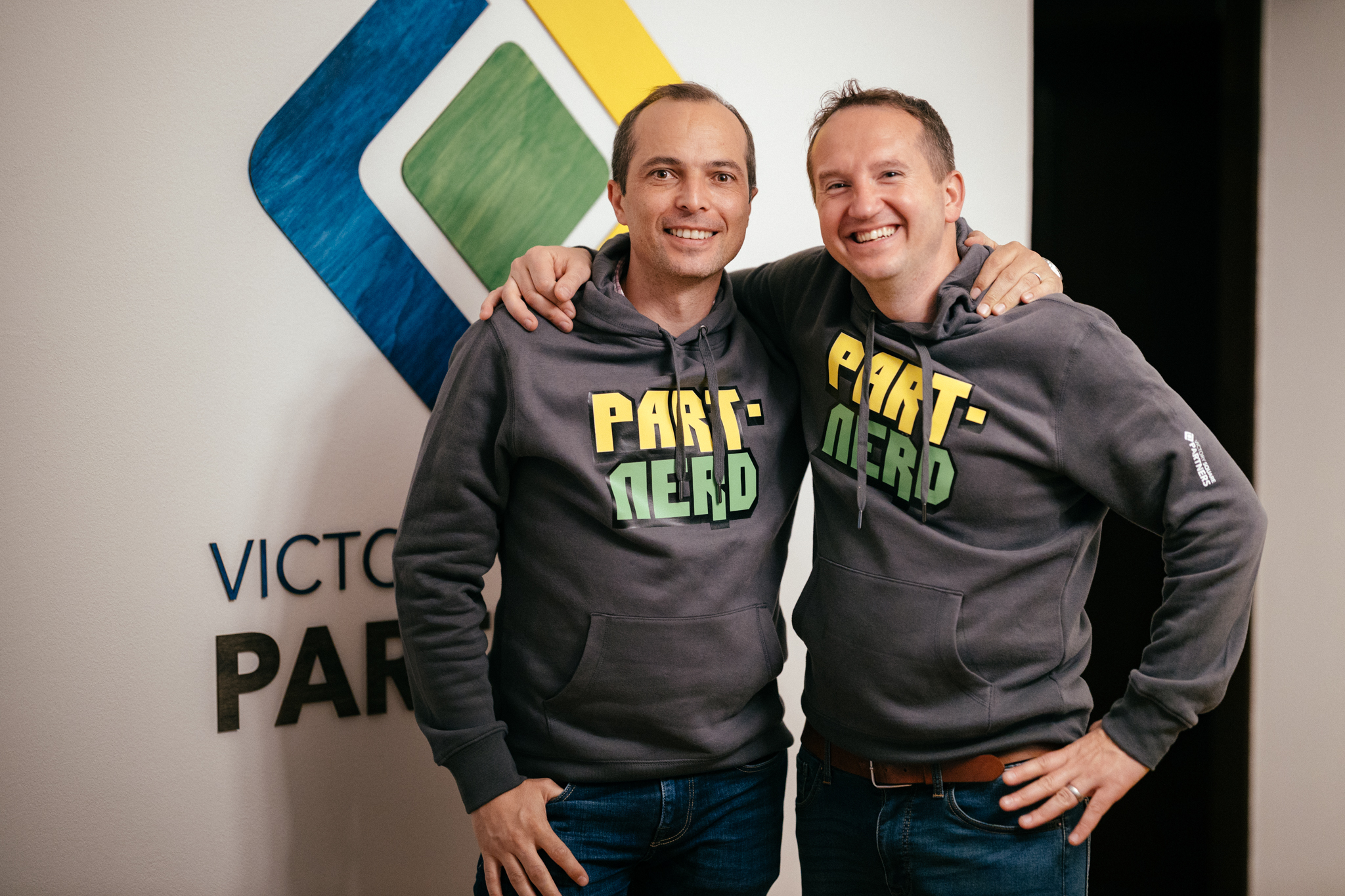 Co-founders of sofware engineering company Victory Square Partners in front of the logo. Both are wearing company hoodies with the text Part.nerds